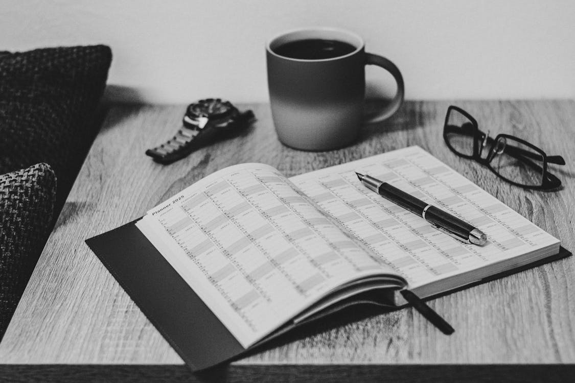 A neatly organised desk with an open daily planner, laptop, and coffee cup, set up for a productive work session